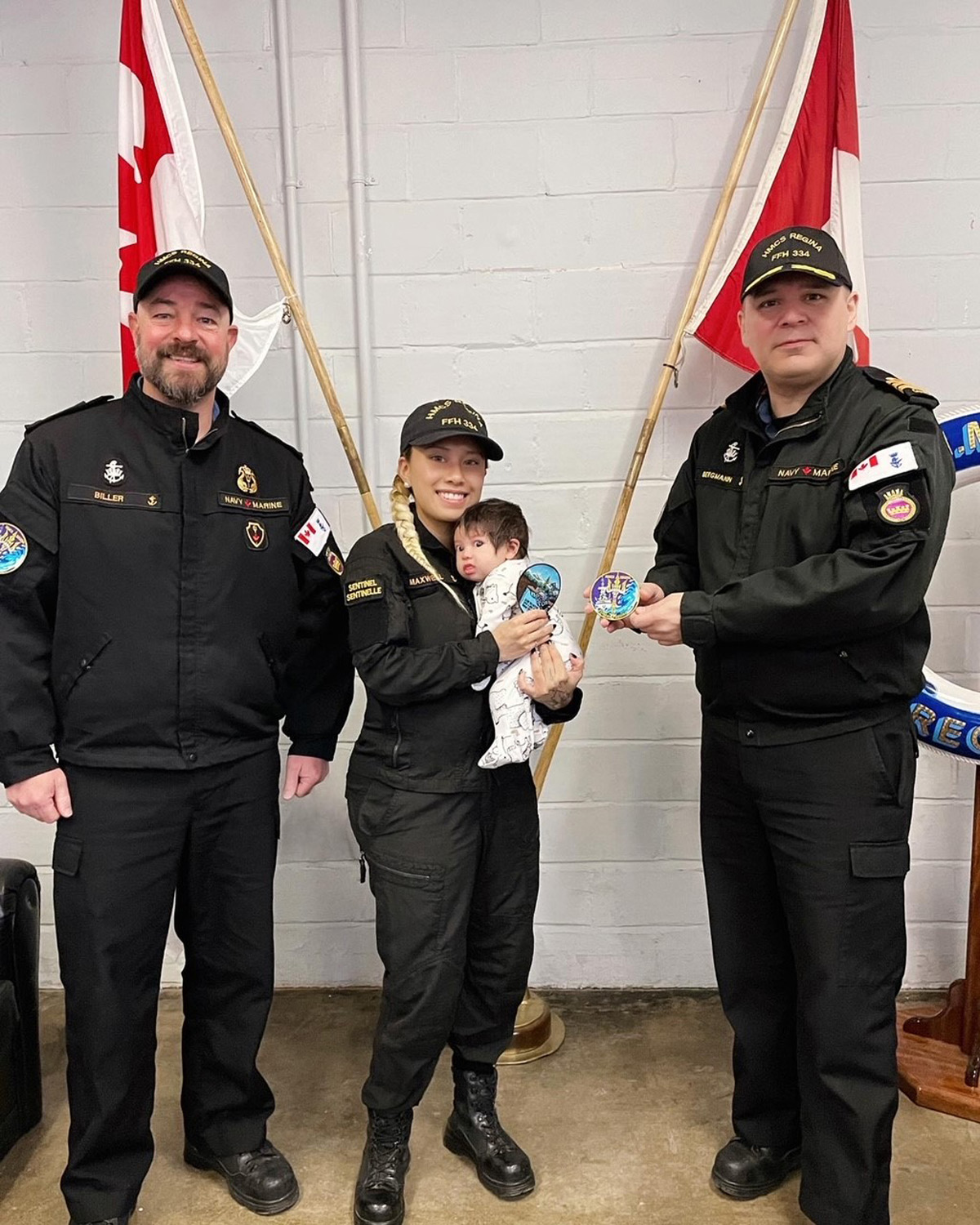 Commander Tyson Bergmann, Regina's Commanding Officer and Chief Petty Officer First Class Ian Biller, Regina's Coxswain, present Sailor First Class Marianne Maxwell (holding newborn daughter Estella) HMCS Regina's morale patch, which she designed.
