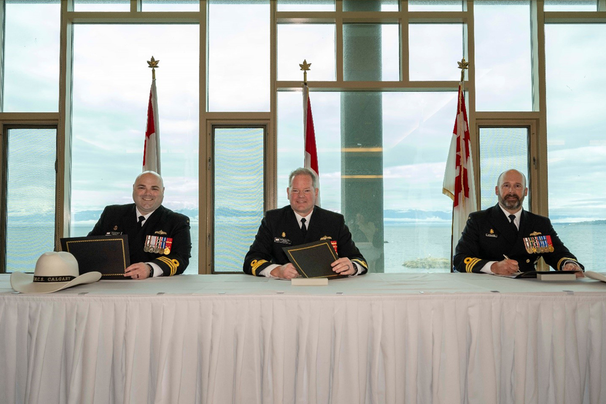 (DE GAUCHE À DROITE) : Le capitaine de frégate Jeremy Samson, commandant sortant, le commodore David Mazur, officier réviseur, et le capitaine de frégate Matthew Woodburn, commandant entrant, signent les documents de passation de commandement lors de la cérémonie de passation de commandement qui s’est déroulée dans la salle Arc-en-ciel du mess des chefs et des officiers mariniers, le 13 mai.