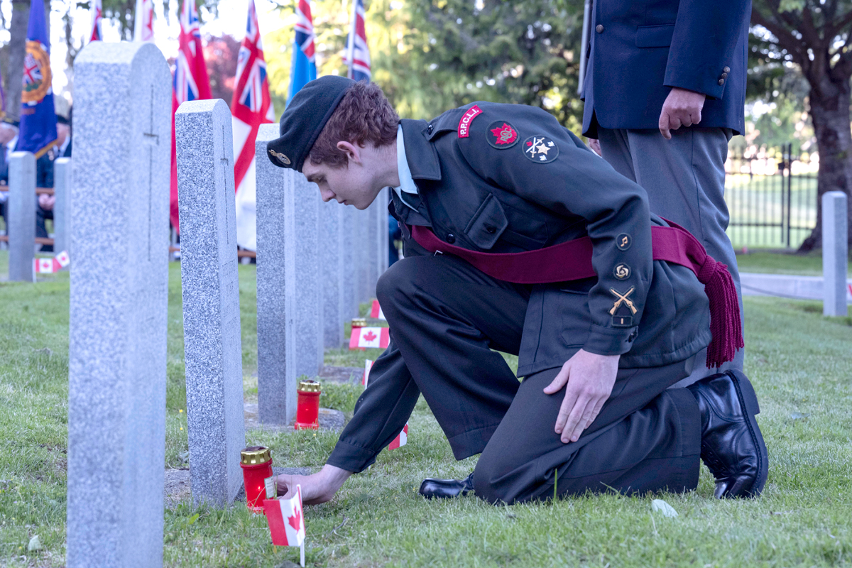 Cadet pays respect by placing a candle near a headstone during the Candleight Tribute.
